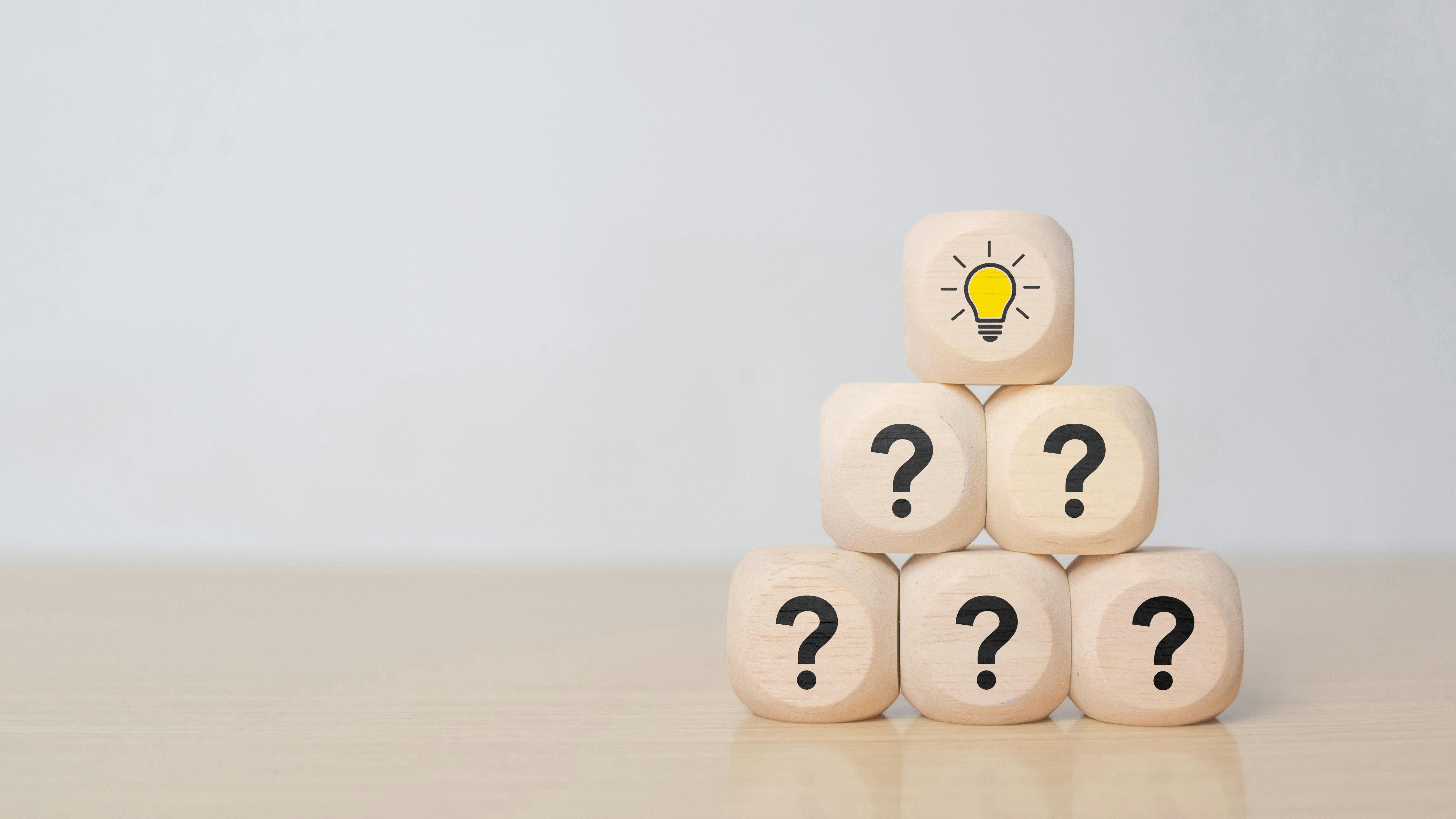 Wooden blocks stacked in a pyramid with question marks, topped by a block with a lightbulb icon