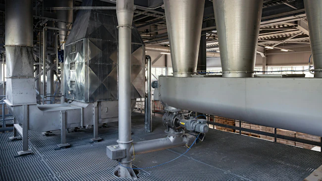 The interior of a modern factory. Large stainless steel hoppers(cyclones) and a screw conveyor(auger) are part of an automated system for conveying bulk powder. The machinery is on a metal grate floor