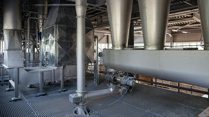 The interior of a modern factory. Large stainless steel hoppers(cyclones) and a screw conveyor(auger) are part of an automated system for conveying bulk powder. The machinery is on a metal grate floor