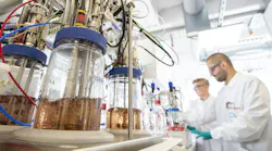 Covestro chemicals in lab with two workers in the background Covestro chemicals in lab with two workers in the background