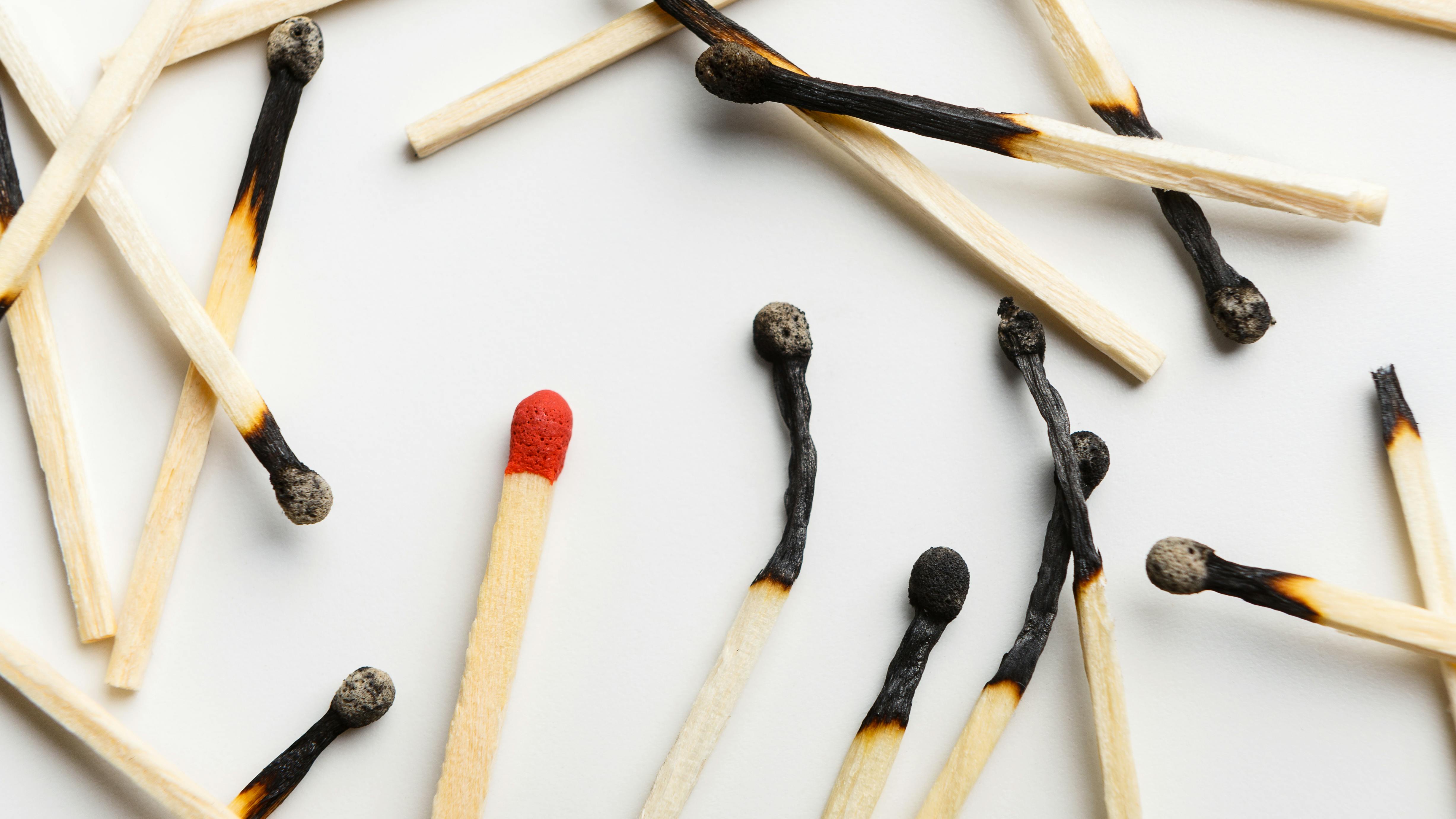 pile of burnt matchsticks with one unlit match on a white background