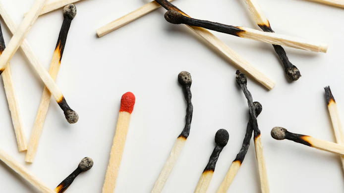 pile of burnt matchsticks with one unlit match on a white background