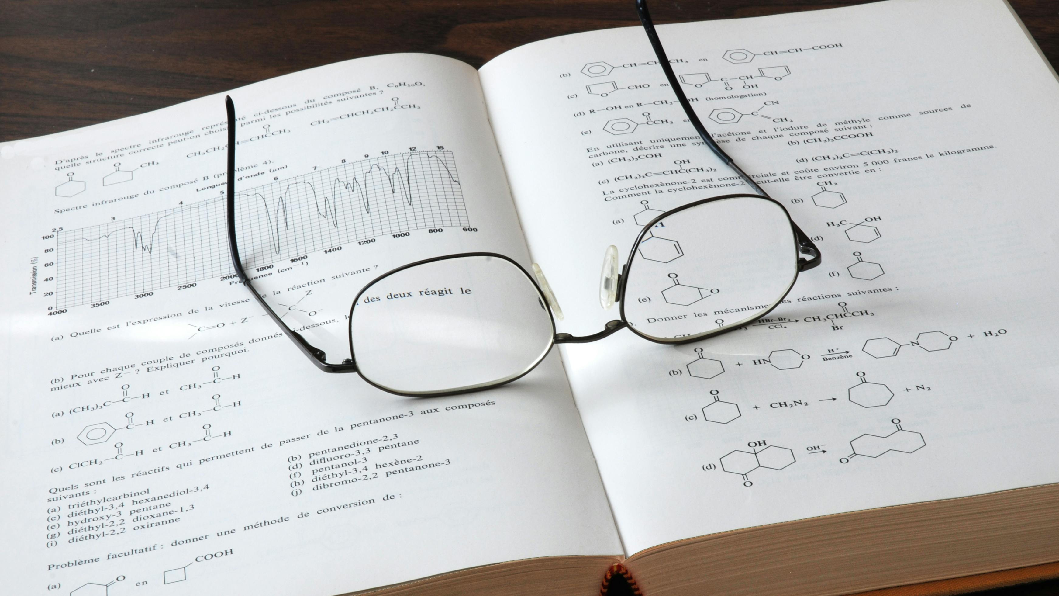 Open chemistry book showing formulas and graphs with eyesglasses on top of the pages