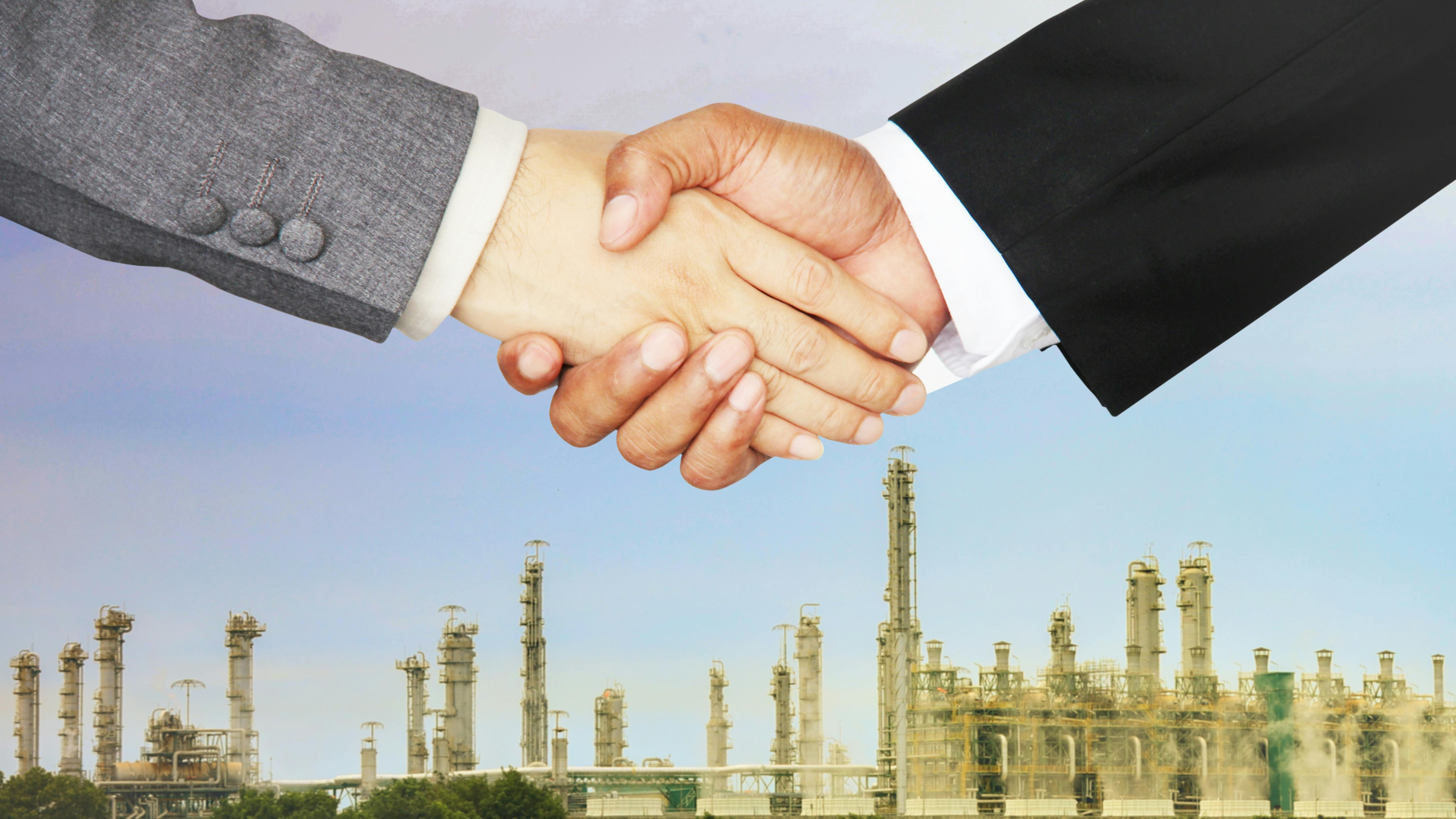 close up of two business men shaking hands with chemical plant in the background