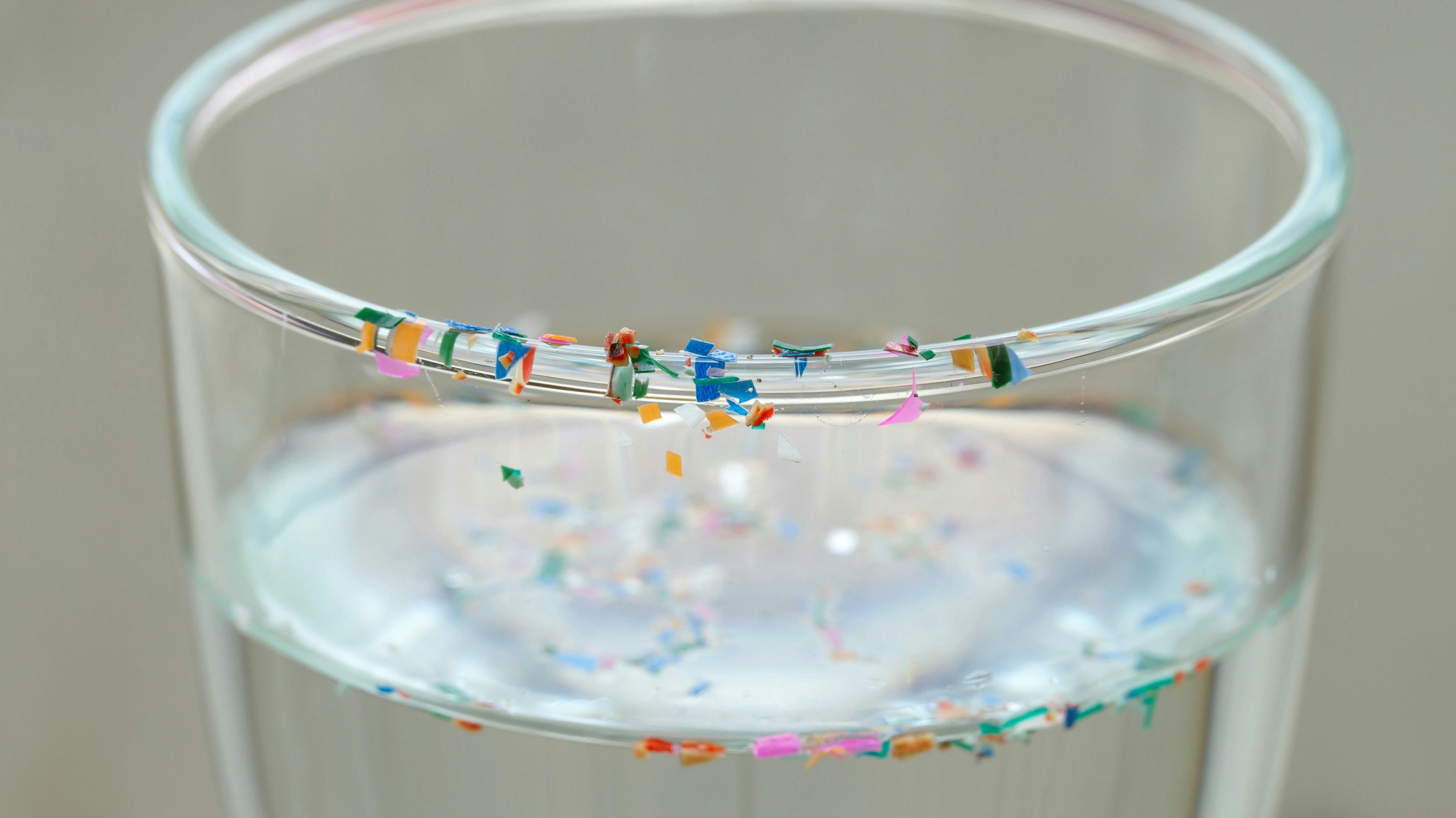 Drinking glass with water and colorful plastic particles floating in the water and sitting along the rim of the glass
