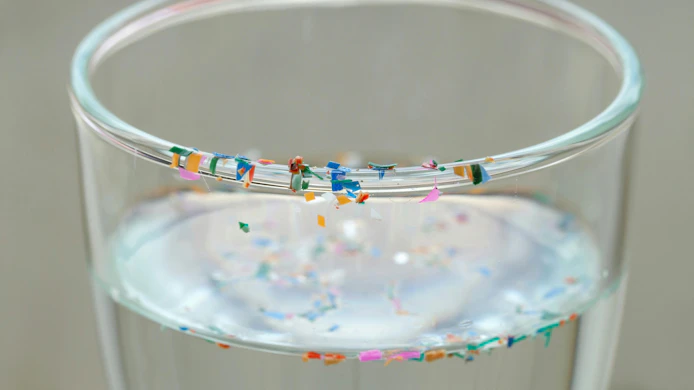 Drinking glass with water and colorful plastic particles floating in the water and sitting along the rim of the glass