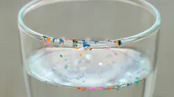 Drinking glass with water and colorful plastic particles floating in the water and sitting along the rim of the glass