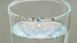 Drinking glass with water and colorful plastic particles floating in the water and sitting along the rim of the glass