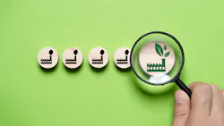 A magnifying glass highlights a green eco-friendly factory icon among polluting factory icons on wooden discs.