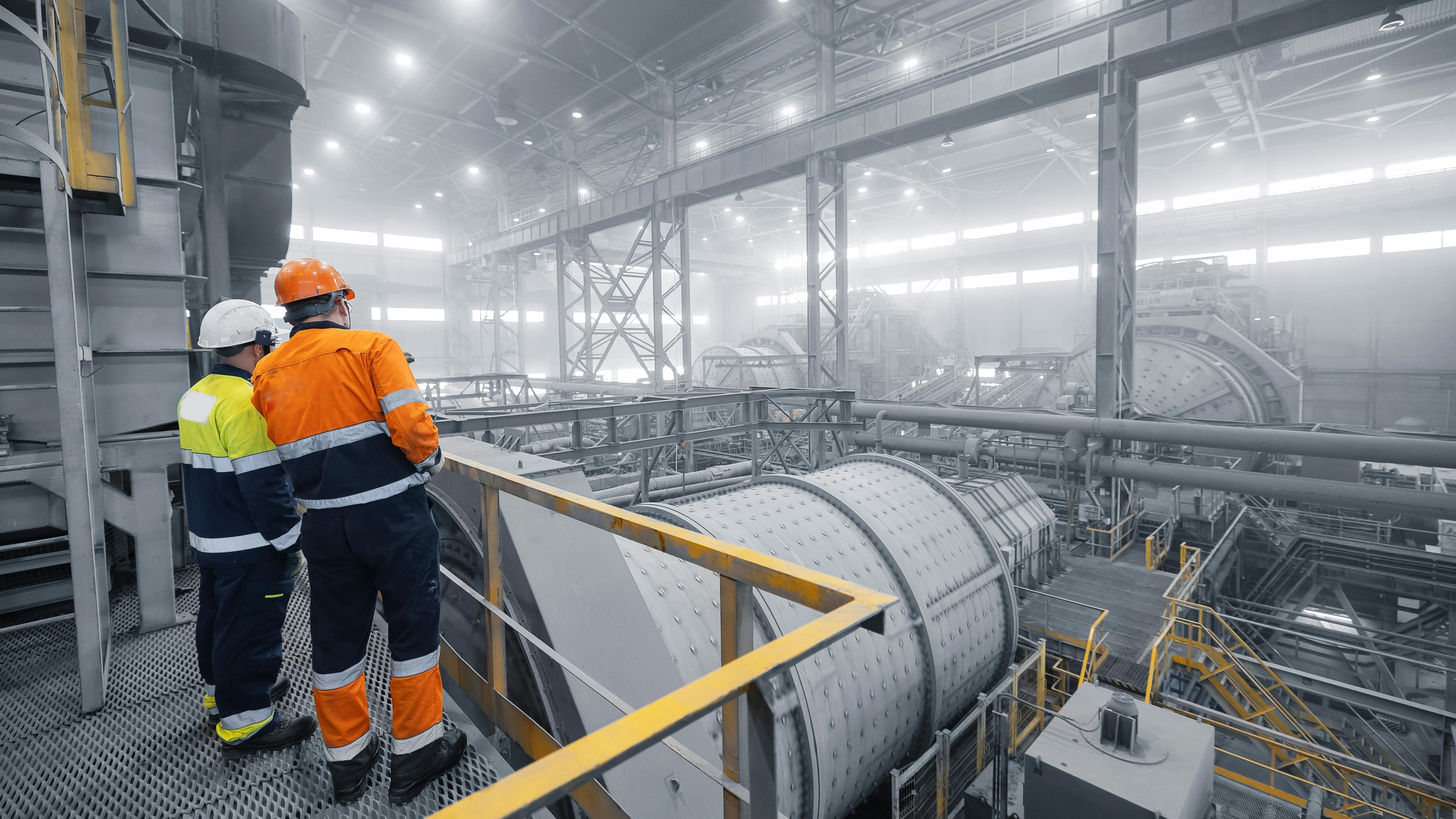 Industrial manufacturing mining workplace. Colleagues having discussion talk cooperation on during working process on background grinding ball mill with mineral gold ore