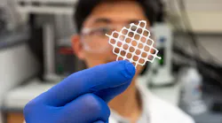 a researcher in a white labcoat and purple gloves holds a piece of white mesh up in front of the camera