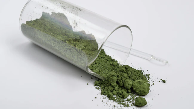 A glass vial on its side partially filled with Chromium III oxide powder