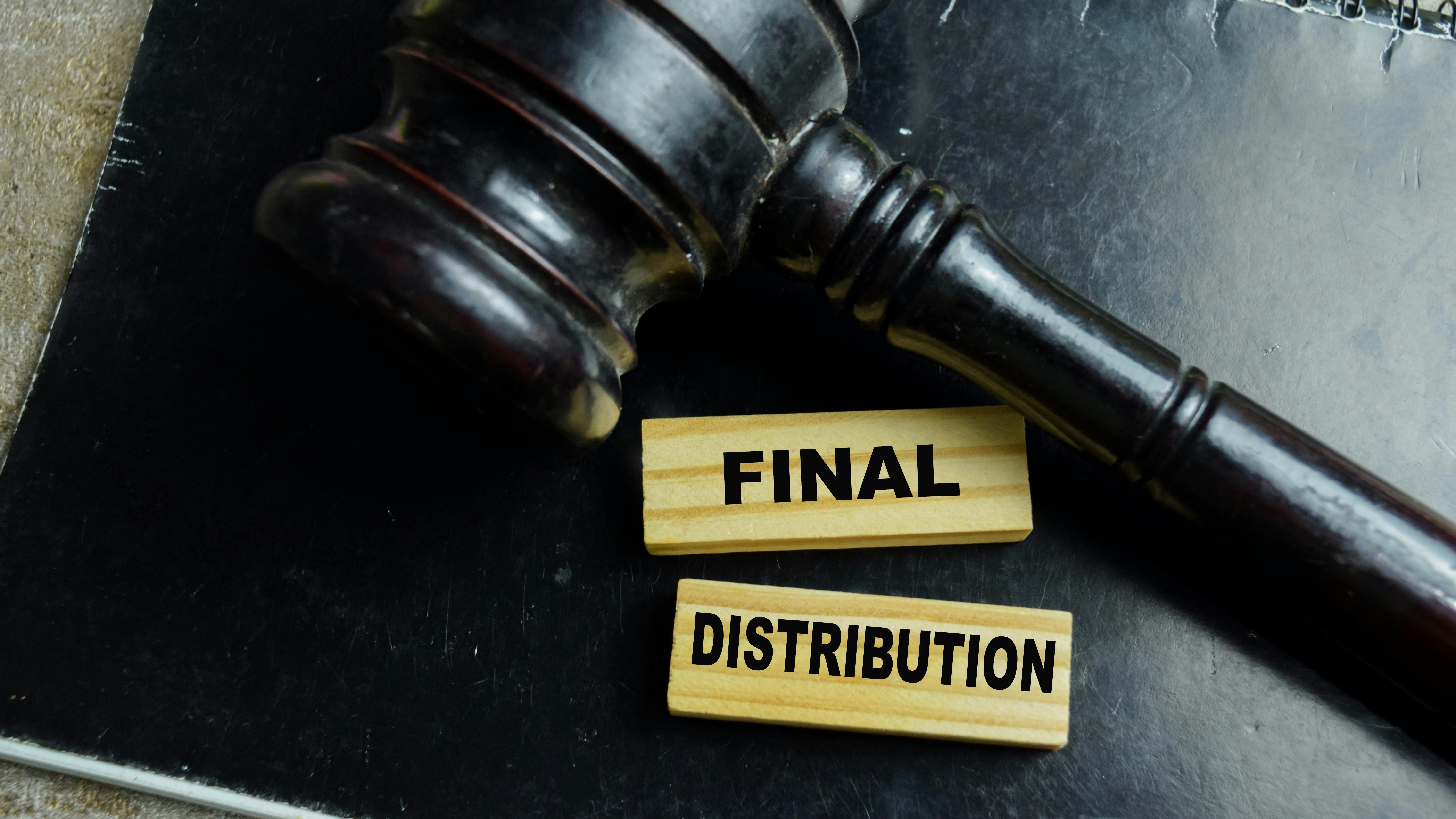 Courtroom gavel sits on top of black leather legal pad and small wooden blocks with the words Final Distribution