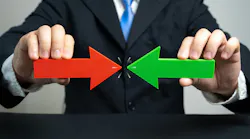 Person in a business suit holds a red arrow and a green arrow pointing toward each other, symbolizing negotiation, alignment, or convergence.