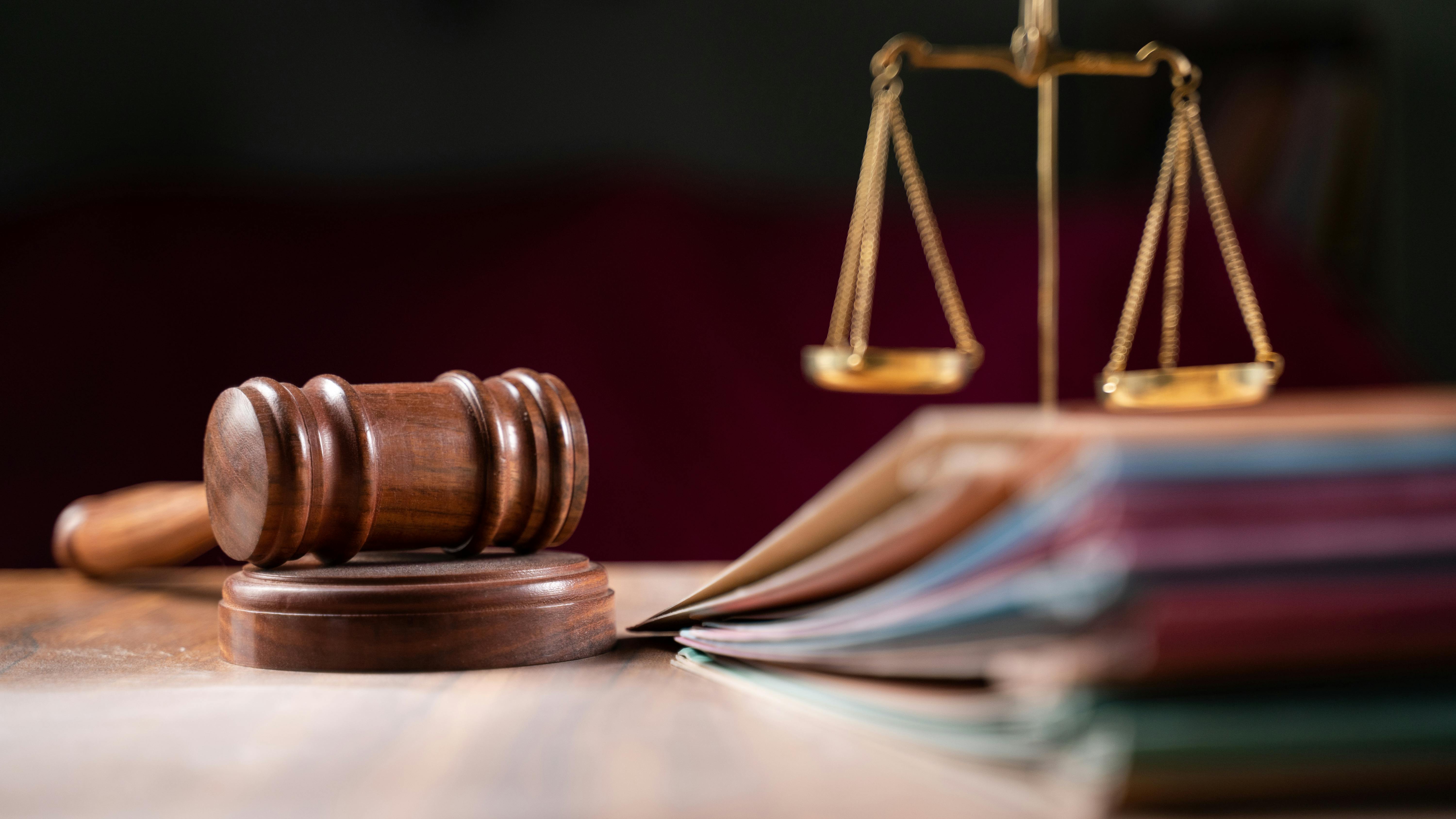 Judge's gavel in focus with legal folders and scale blurred in background