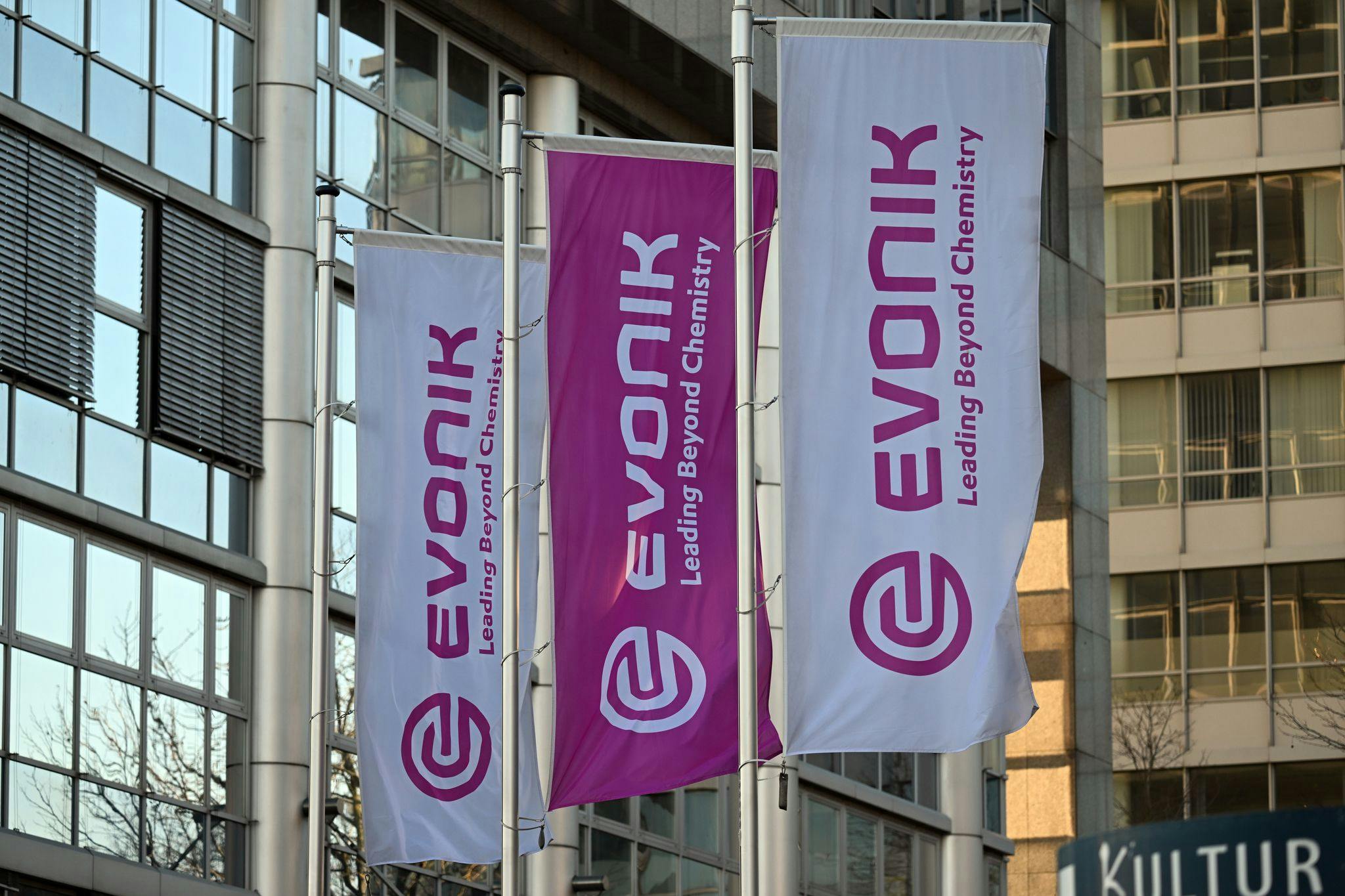 Flags bearing Evonik's corporate logo fly in front of the company's headquarters.