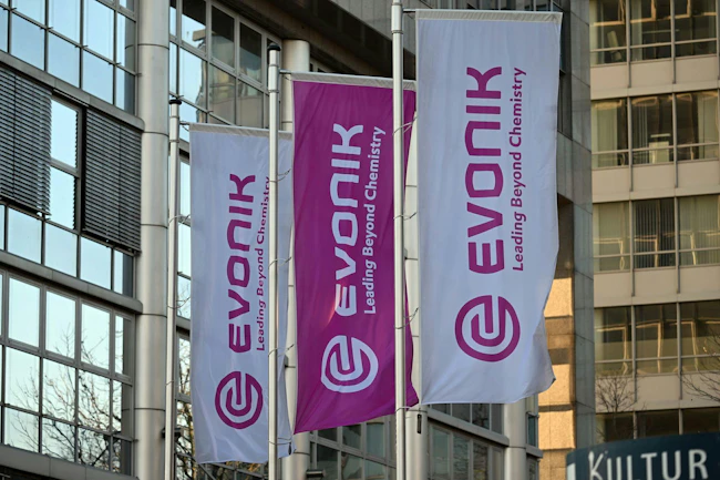 Flags bearing Evonik's corporate logo fly in front of the company's headquarters.
