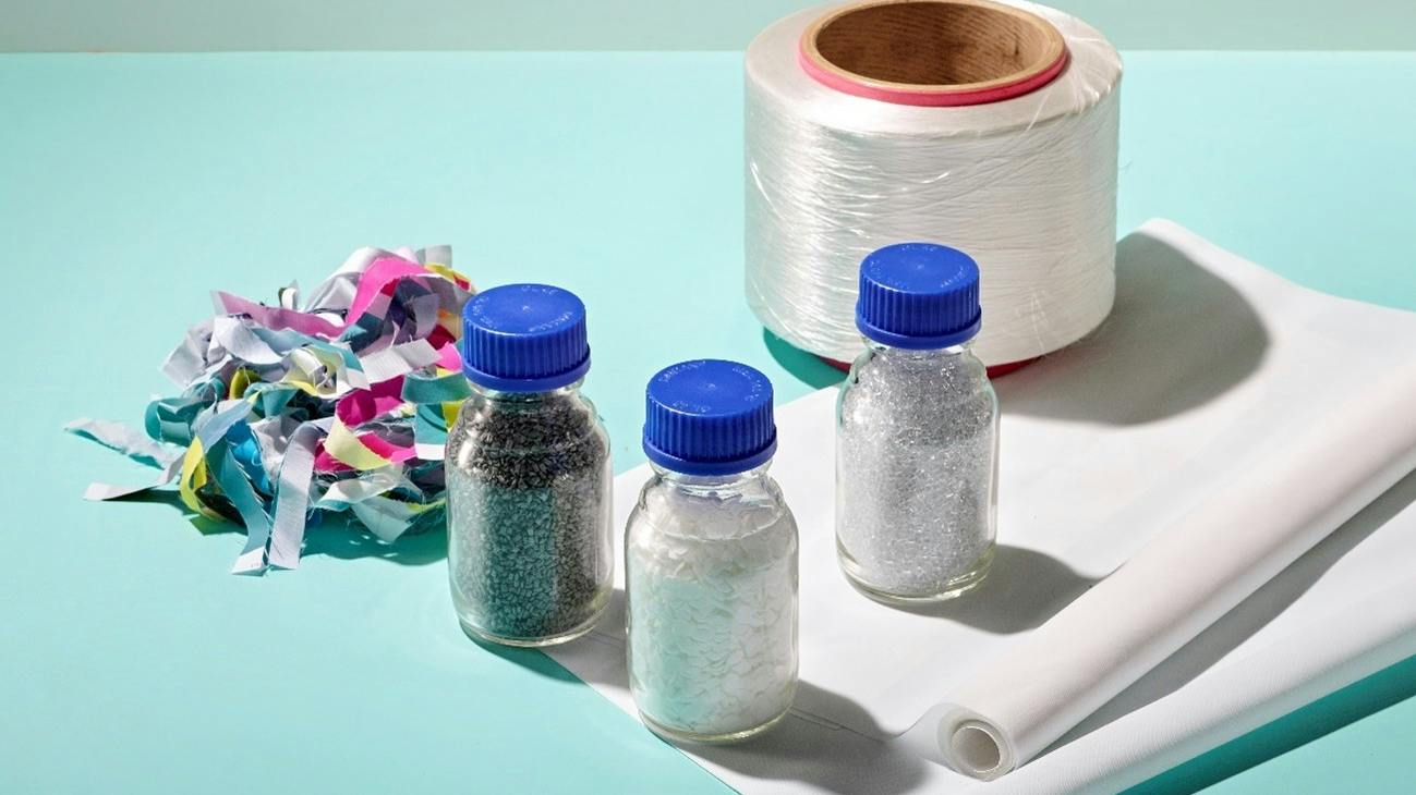 Products from each stage of the process, in which waste banners are finely shredded, chemically recycled into recycled materials, spun into yarn, and made into banners.
